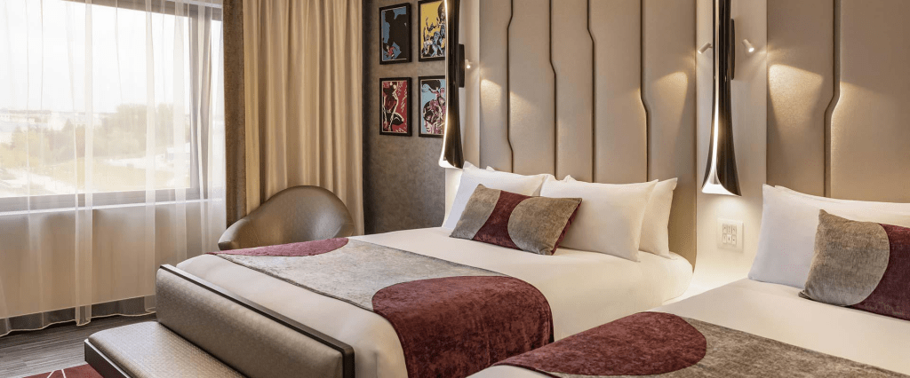 Interior of a hotel bedroom with two beds and art work on the walls a well as a large window 