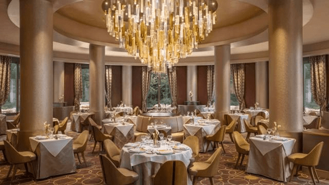 A picture of a restaurant dining room set for dinner with a beautiful chandelier in the centre 